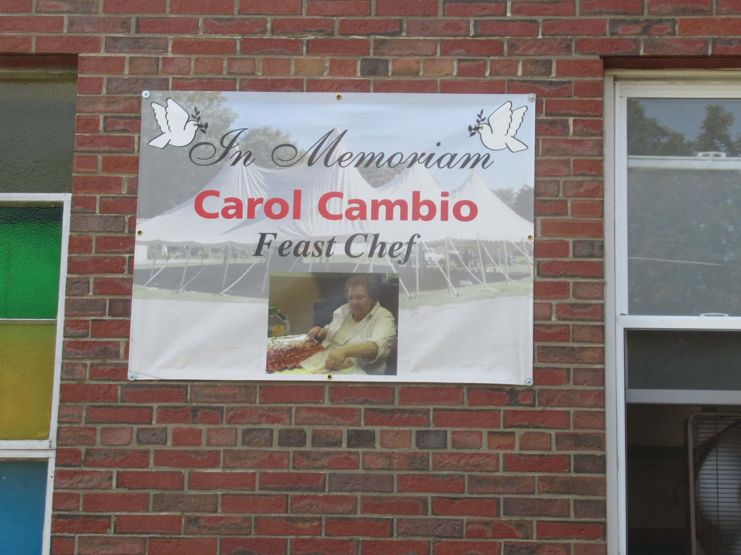 SPECIAL SALUTE: Carol Cambio, the long-serving chef for Our Lady of Grace Church’s Feast and Festival, is remembered by this memorial sign that’s attached to the wall by the entrance to the parish.